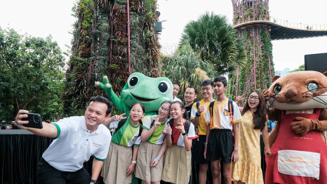 Senior Minister of State for Ministry of Defence and Ministry of Sustainability and the Environment Mr Zaqy Mohamad (left) taking a selfie with participating students, National Environment Agency Group Director (Public Engagement Group) Mr Lim Yuin Chien (in white), Gardens by the Bay CEO Mr Felix Loh (in black), and Biogirl MJ (in yellow dress), alongside National Environment Agency mascot Captain Green and Singapore Food Agency mascot Oscar at Race to Sustainability!.